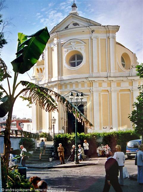 Yellow and white church with curved facade, square with people and banana plant