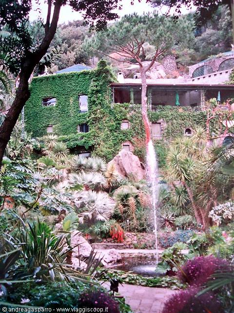 Ivy-covered building among palms and pines, water jet in the garden