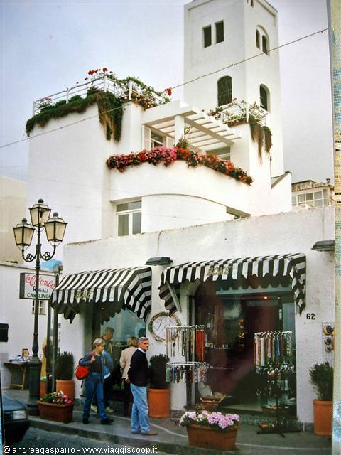 Shoppers by striped-awning shops beneath the white tower in Anacapri