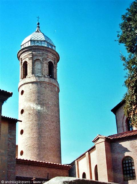 Round brick bell tower with dome beside tiled rooftops under a clear blue sky