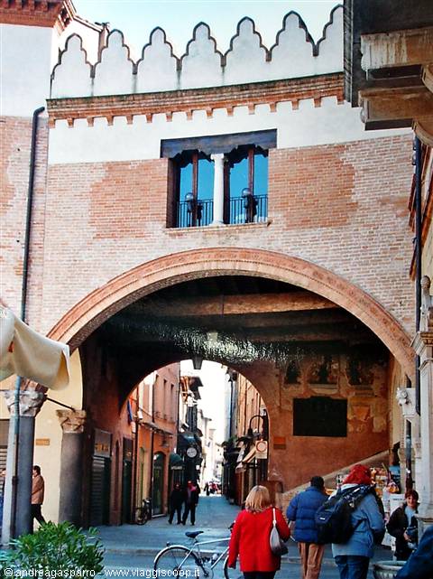 Old brick archway with crenellations, pedestrians and bicycle in the street