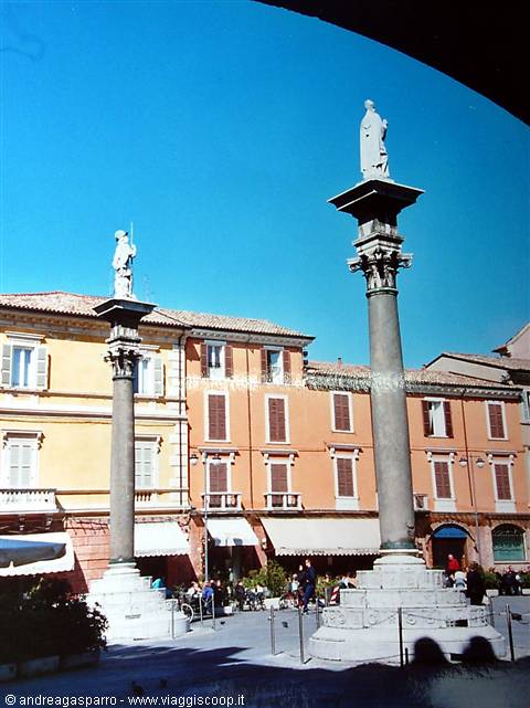 Columns with statues in Piazza del Popolo, Ravenna, colorful buildings under blue sky