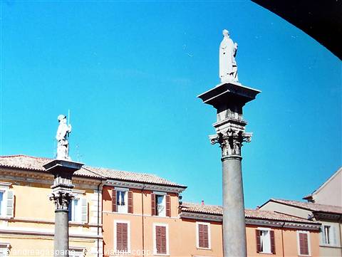 Columns topped with saint statues in sunny square, ochre houses, Ravenna
