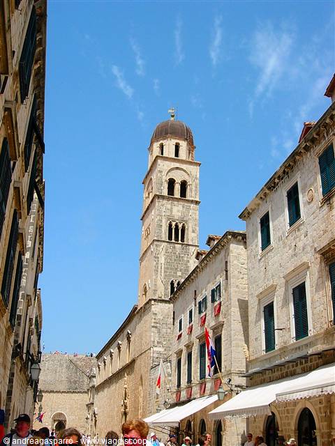 Stone bell tower over Dubrovnik's Stradun, tourists among flags and awnings