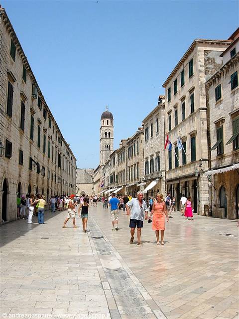 Tourists walk along Dubrovnik's Stradun past stone buildings and the bell tower