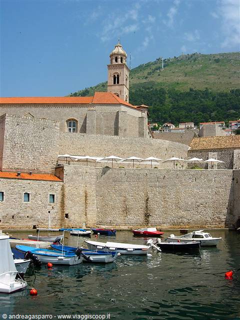 Boats in Dubrovnik old harbor beneath stone walls and bell tower