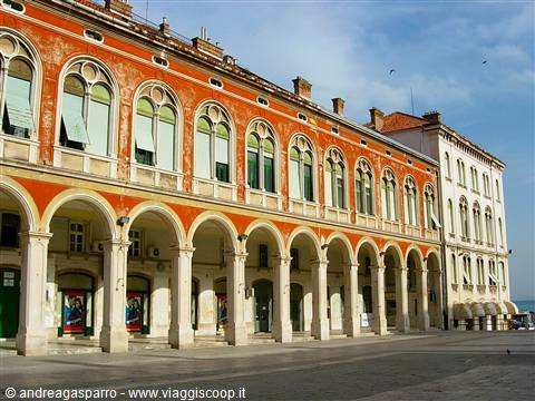 Arcaded orange building with round arches in a sunny square, Trieste