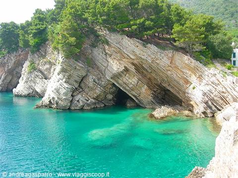 Layered rocky cliff over turquoise water, green pines on the rocks