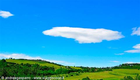 White cloud above lush green hills with fields and woods