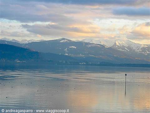 Buoy on calm lake water, snowy Alps glowing under cloudy sky