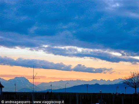Blue and golden clouds over snowy mountains, antennas and lampposts in silhouette