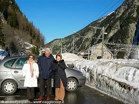 Three people beside a car in the snow near a mountain railway station