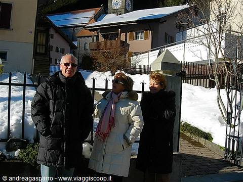 Three people in winter jackets in front of snowy houses and church steeple