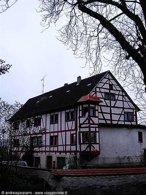 Half-timbered house with red beams and oriel window under bare tree branches