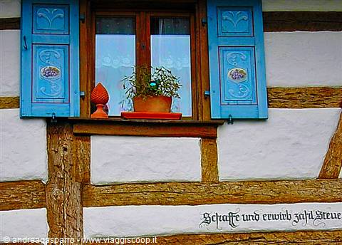 Window with painted blue shutters on half-timbered wall with proverb