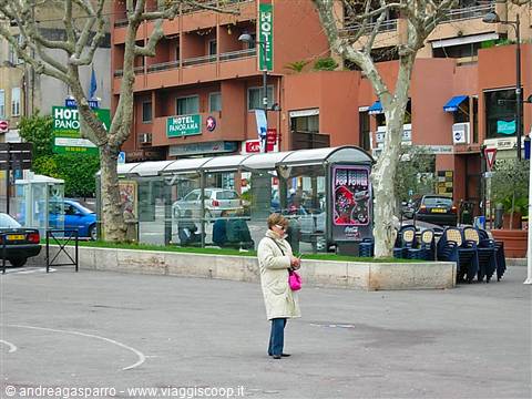 Woman in cream coat crossing the square in front of hotels, Menton