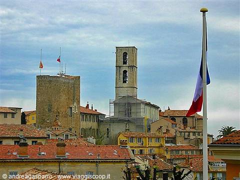 Bell tower and medieval tower above tiled rooftops, French flag waving in foreground