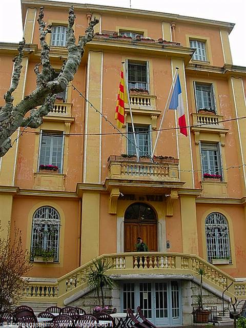 Ochre town hall facade with French and Catalan flags, man at wooden entrance