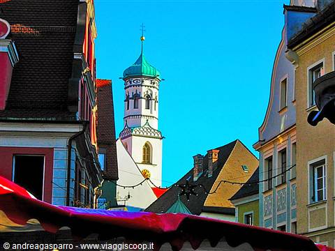 White bell tower with green dome among colorful rooftops and market awnings