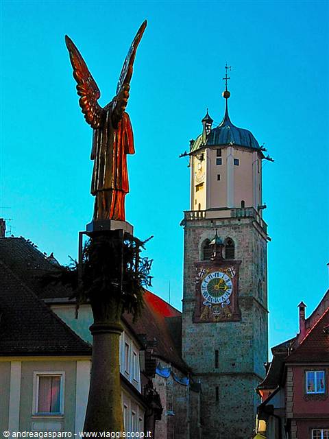 Golden winged statue in front of Memmingen's clock tower, clear blue sky