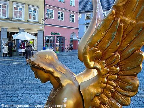 Gilded angel statue on cobbled square with colorful facades