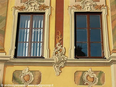 Baroque painted facade with two wooden windows and golden stucco decorations