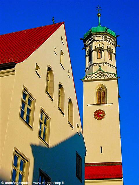 White clock tower with green dome beside a cream building under blue sky