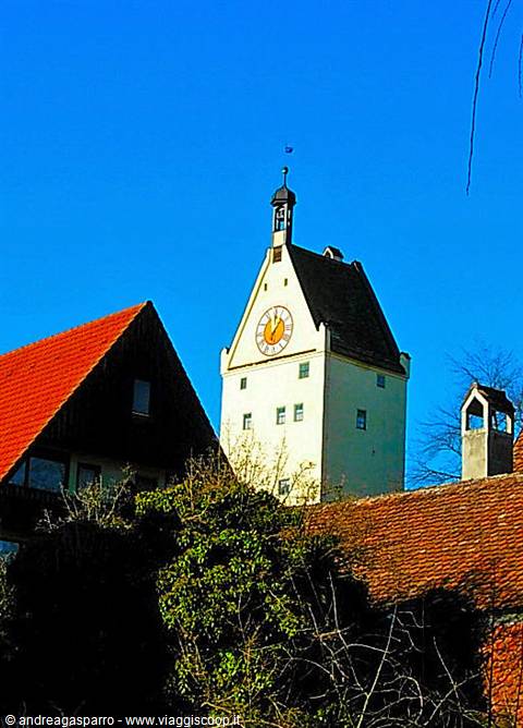 White clock tower with golden clock and black roof above red rooftops