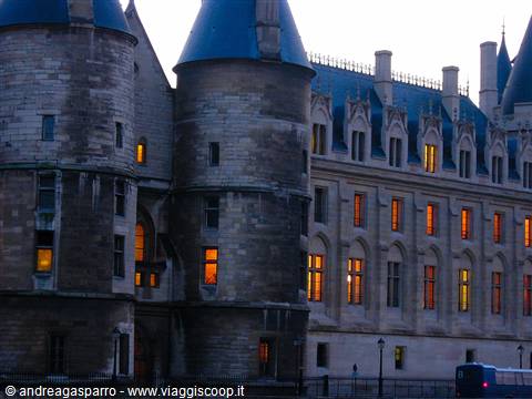 Stone towers of the Conciergerie in Paris with lit windows at dusk