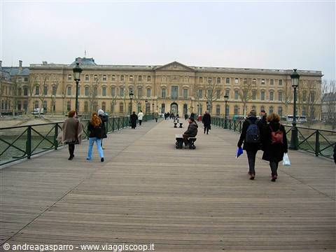 Visitors walk across the wooden Pont des Arts toward the Louvre under a grey sky