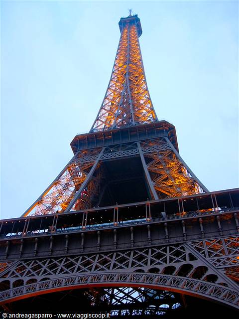 The Eiffel Tower glowing orange at dusk, seen from below