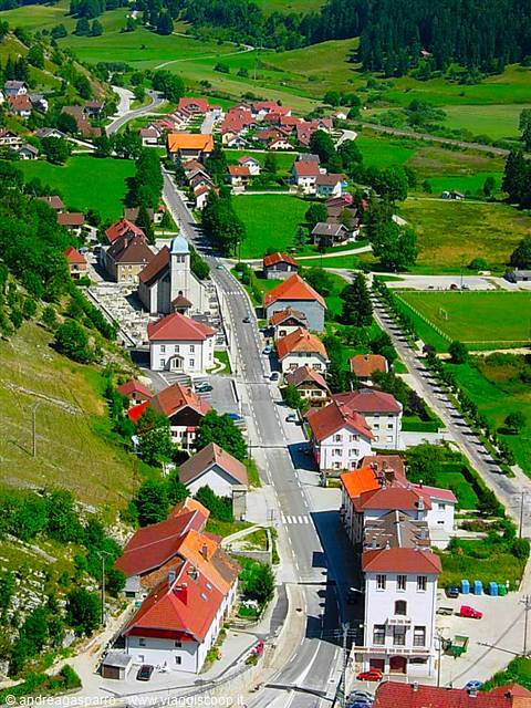 Mountain village with red roofs, main road and church among green meadows