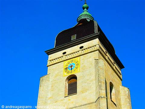 Light stone bell tower with yellow clock and dark dome against blue sky