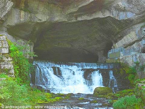 Waterfall flowing from a large rock cave, green moss and walkway