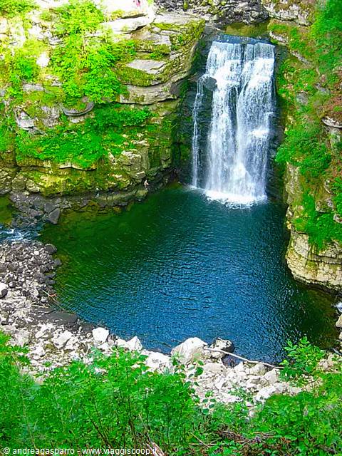 White waterfall over mossy rocks, turquoise pool in a green gorge