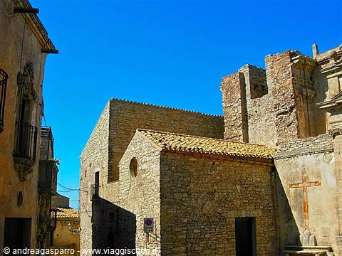 Stone church with painted cross beside ruins, old village under blue sky