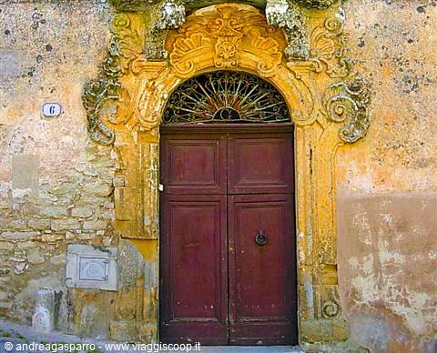 Baroque carved yellow stone portal with red wooden door, Sicily