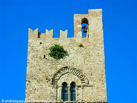 Medieval stone bell tower with battlements, mullioned window and bell, blue sky