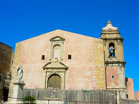 Pink church with stone bell tower and statue in Erice under blue sky
