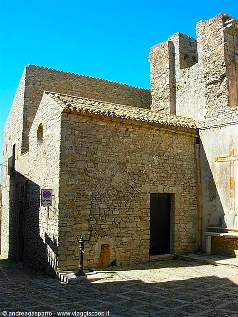 Small stone church with dark doorway on cobbled square, blue sky