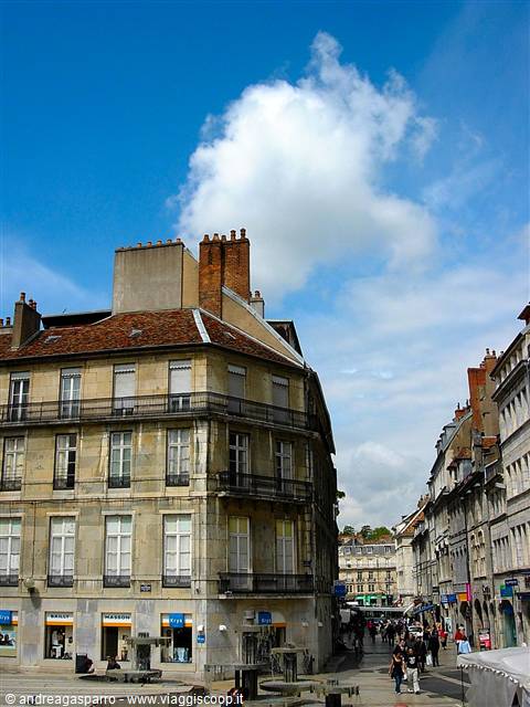 Stone building with tiled roofs, pedestrians under a large cumulus cloud