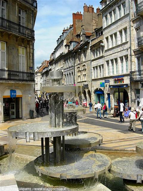 Stone fountain on pedestrian square with old buildings and passersby, Besançon