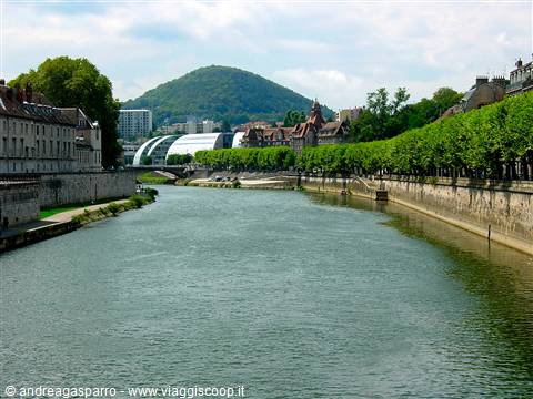 The Doubs river in Besançon between stone walls, trees and a green hill