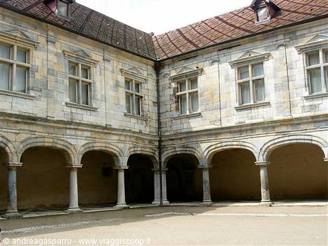 Courtyard arcade with stone columns and mullioned windows under tiled roof