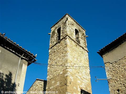 Medieval stone bell tower between old houses, blue sky