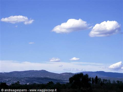 White clouds over dark hills and trees in the foreground