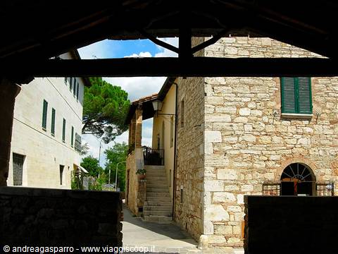 Alley between stone houses with green shutters, seen from under a porch
