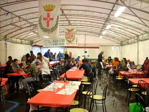 Tent hall with banners, red-clothed tables, people eating and waitress in white apron