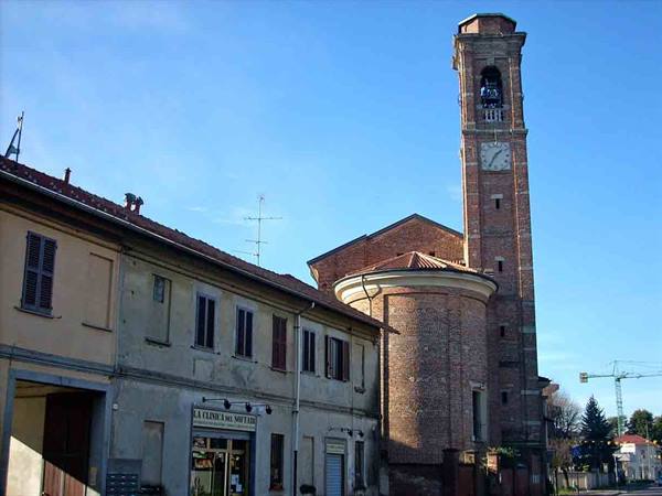 Brick bell tower with clock beside yellow houses under blue sky