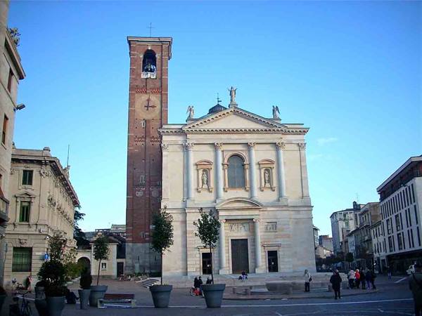 White church with brick bell tower, people in the square under blue sky